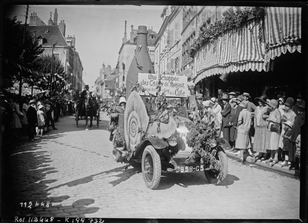 Char automobile décoré d'une bouteille géante et d'un escargot, défilant devant une foule