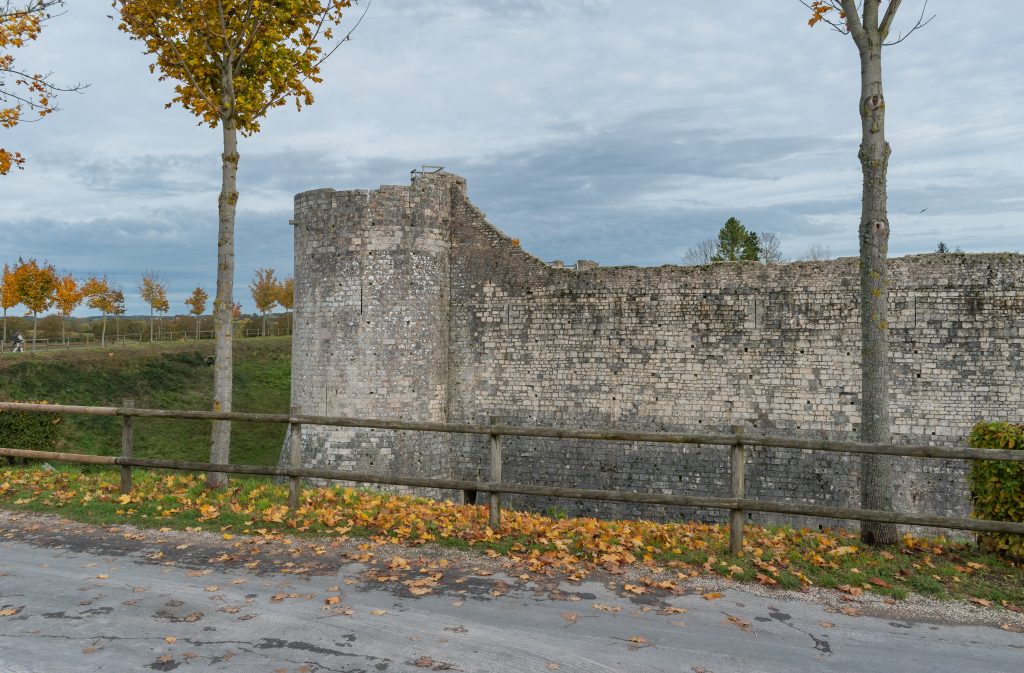 Remparts médiévaux en pierre et tour ronde derrière une barrière de bois, feuilles automnales