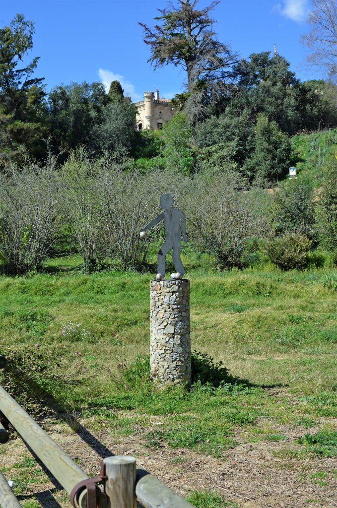 Silhouette métallique de joueur de pétanque sur une colonne en pierre, prairie verte