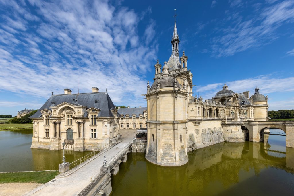 Exterior view of the Château de Chantilly with the bridge and the cour de la capitainerie, from the Terrasse, a sunny day with blue sky, in Chantilly,