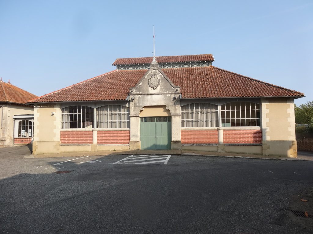 Salle des fêtes en brique et pierre, porte verte, toit de tuiles, parking devant