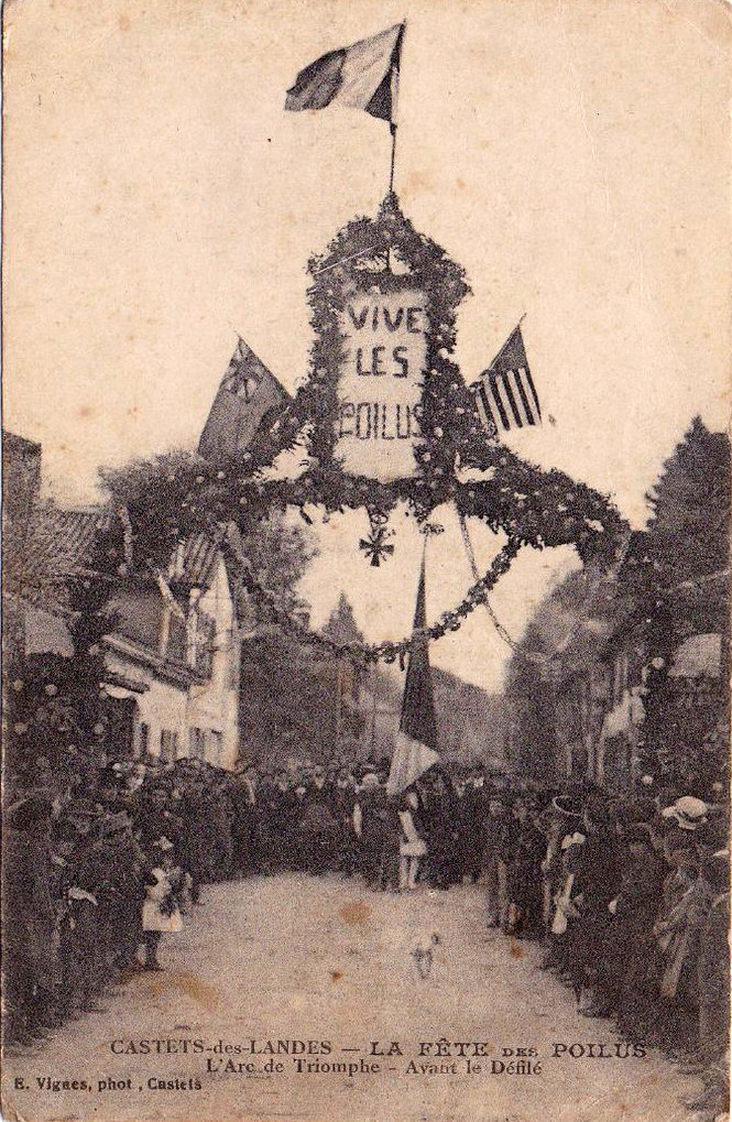 Arc de triomphe fleuri « Vive les Poilus » et foule dans une rue de village