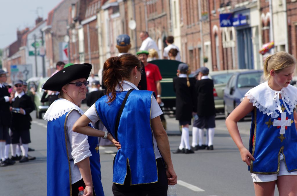 Participants en tabards bleus de mousquetaires attendant dans une rue de village avant le défilé