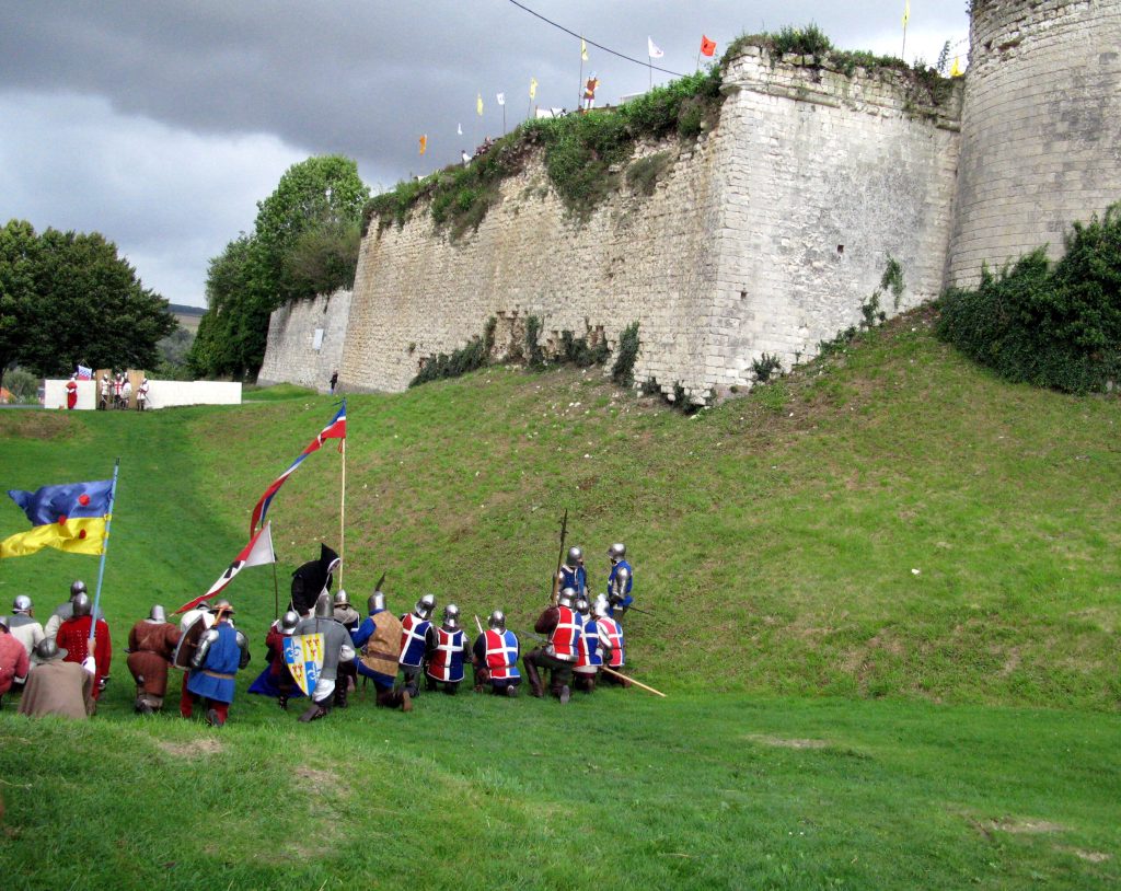 Troupe de soldats médiévaux en armure et bannières devant les remparts d'un château fort