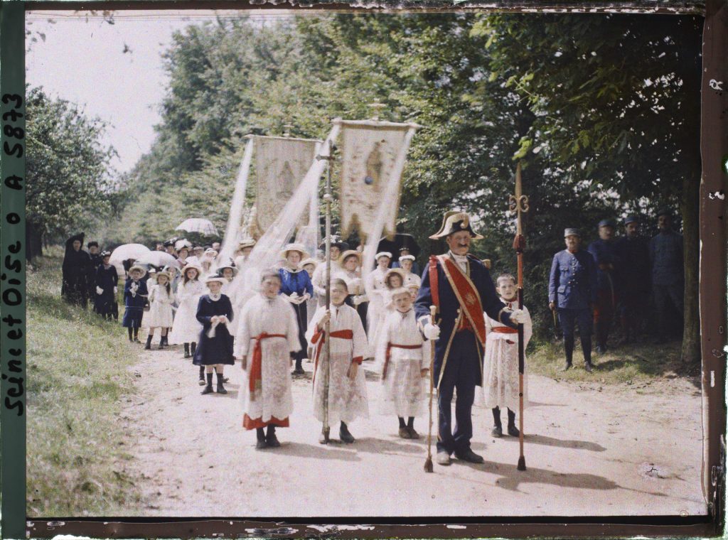 Procession religieuse ancienne sur un chemin, enfants de chœur, bannières brodées et suisse en bicorne