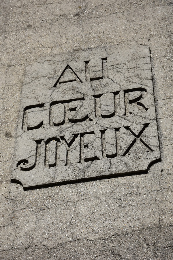 Plaque de pierre gravée « Au cœur joyeux » scellée dans un mur crépi