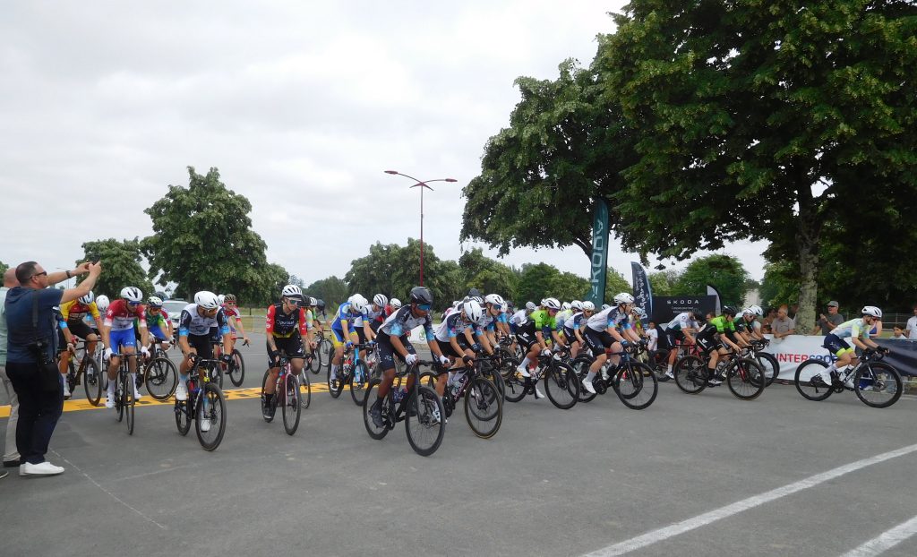 Peloton de cyclistes au départ d'une course sur route, spectateurs et arbres en arrière-plan