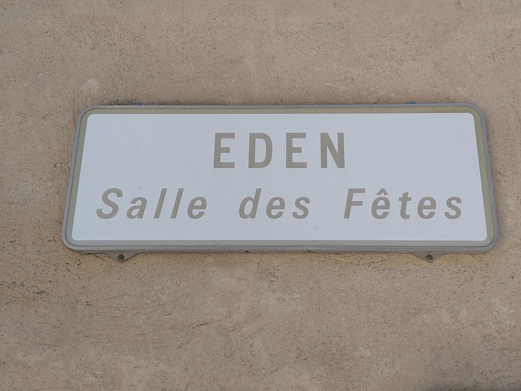 Panneau blanc « EDEN Salle des Fêtes » fixé sur un mur en pierre claire