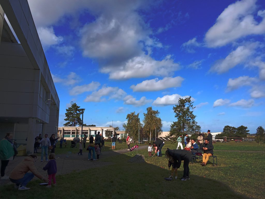 Familles et enfants rassemblés sur une pelouse près d'un bâtiment, sous un ciel bleu