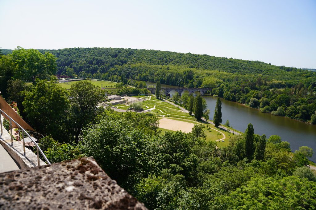 Vue en hauteur sur une rivière bordée de collines boisées, parc aménagé et pont