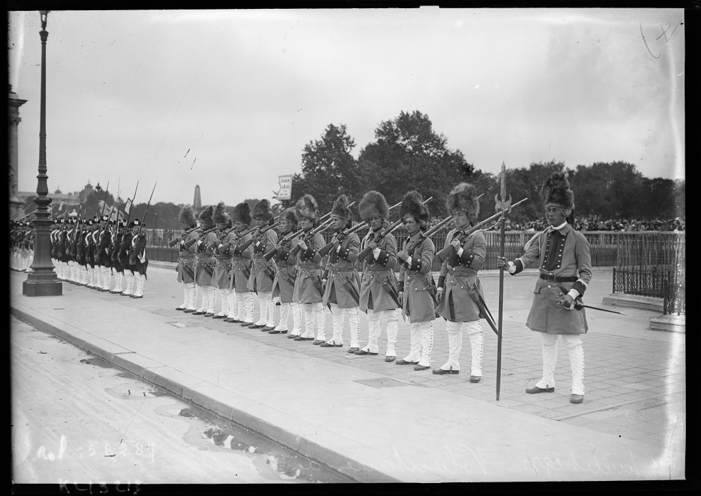 Soldats en uniforme ancien et bonnets à poils alignés fusil à l'épaule lors d'un défilé