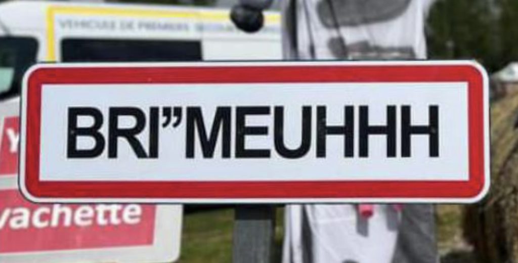 Panneau d'entrée de village détourné affichant « BRI"MEUHHH » devant un véhicule de secours