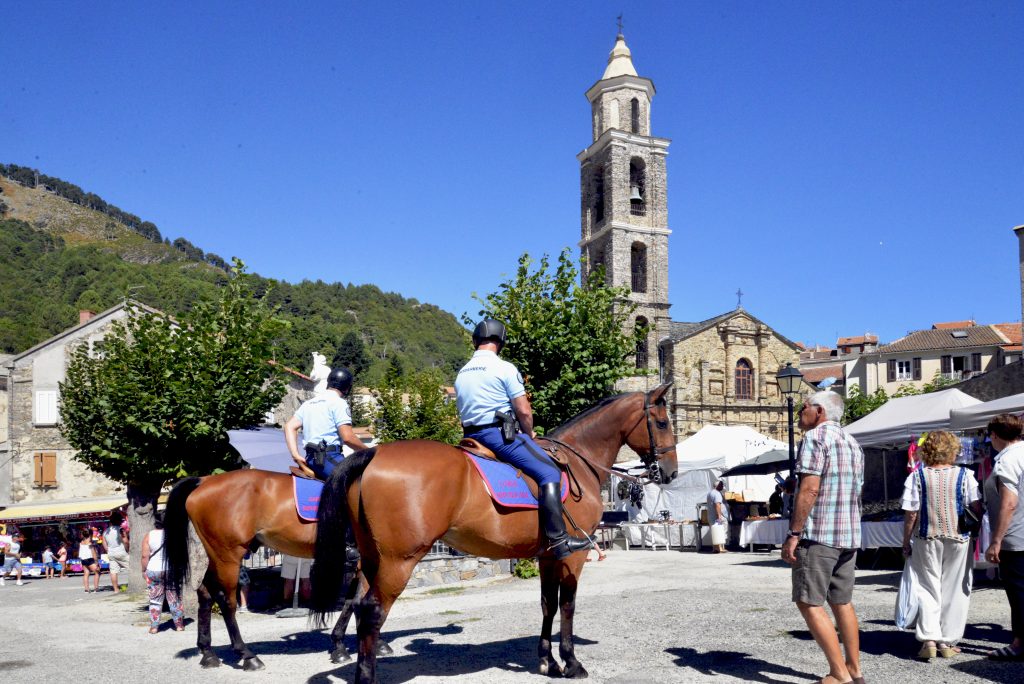 Deux gendarmes à cheval sur une place de marché de village, clocher en pierre