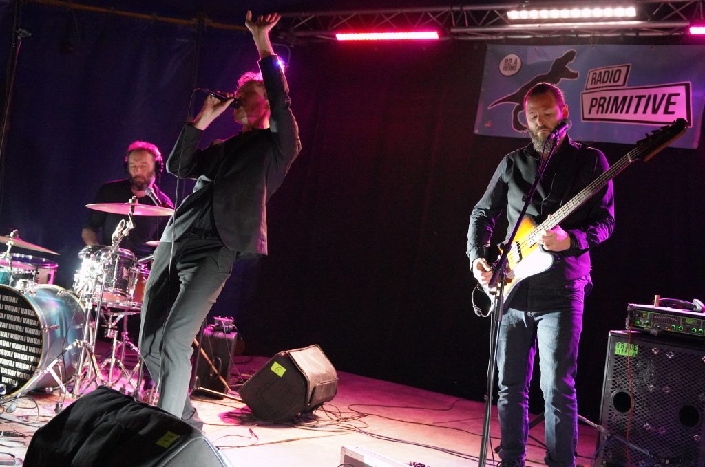 Trio rock sur scène éclairée en rose, chanteur au micro, bassiste et batteur