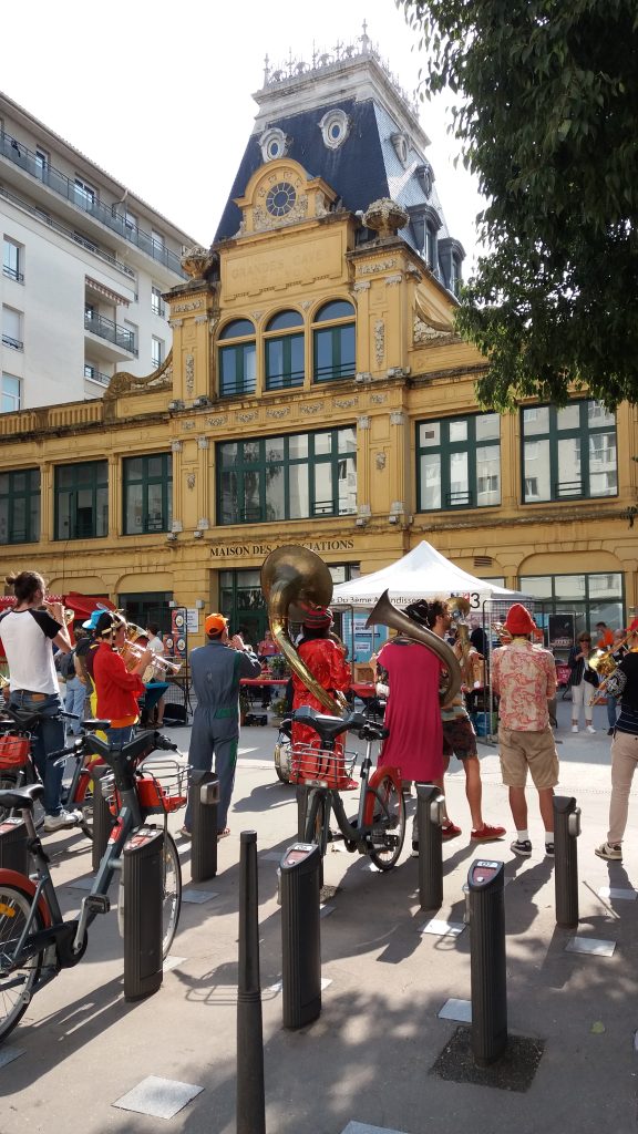Fanfare en tenue rouge jouant devant la Maison des associations, vélos en libre-service au premier plan