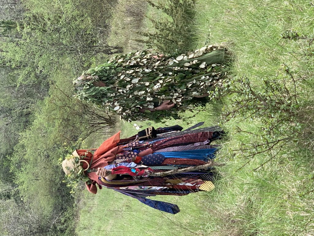 Deux personnages costumés, l'un couvert de feuillage, l'autre de cravates, marchent dans un pré