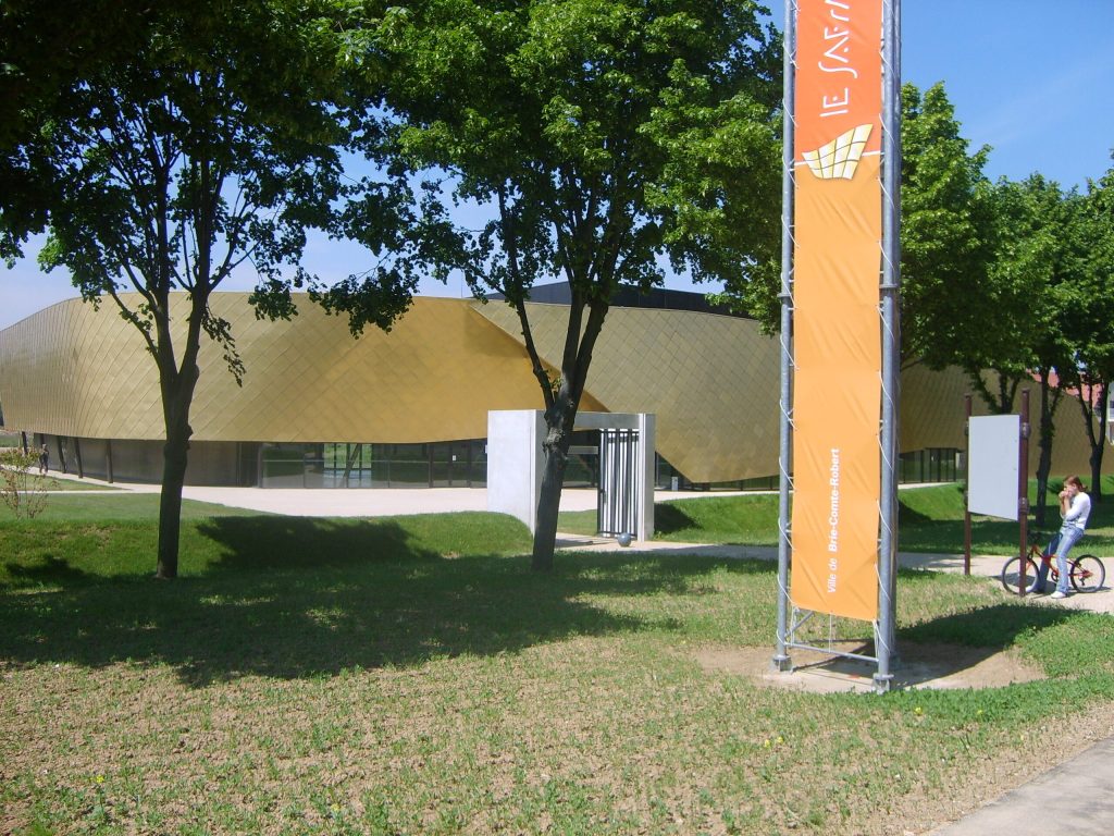 Bâtiment moderne à façade dorée derrière des arbres, oriflamme orange de Brie-Comte-Robert