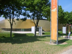 Bâtiment moderne à façade dorée derrière des arbres, oriflamme orange de Brie-Comte-Robert