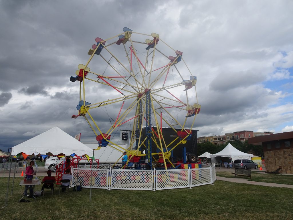 Petite grande roue foraine colorée sur une pelouse, chapiteaux blancs et ciel nuageux