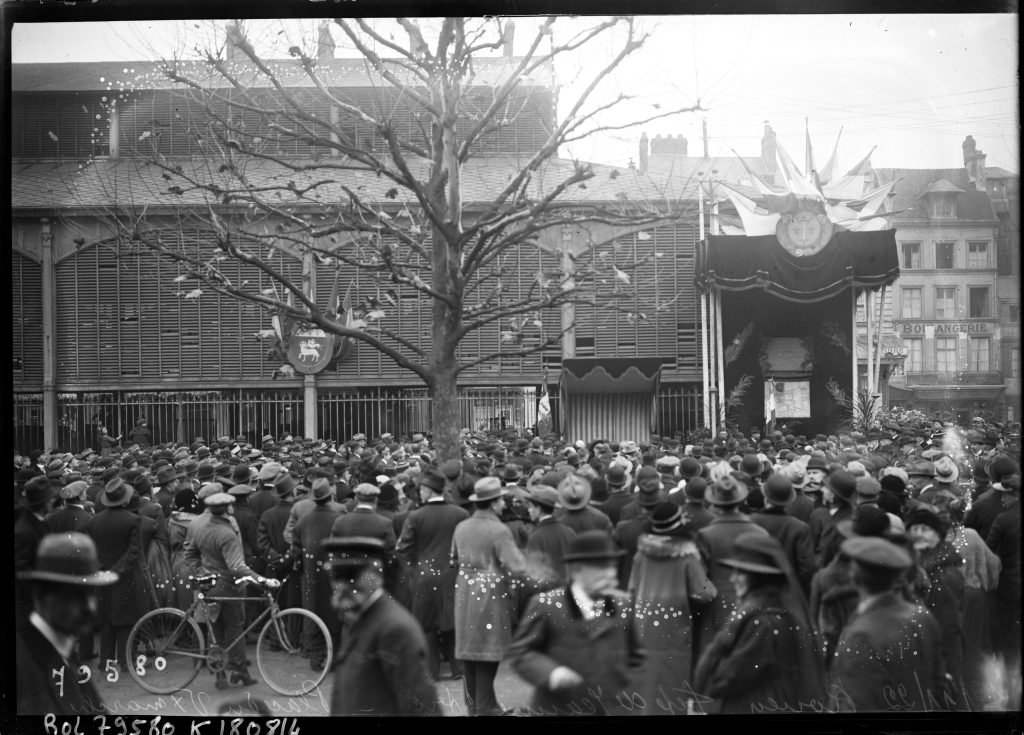 Foule en manteaux et chapeaux devant une halle pavoisée, photo ancienne noir et blanc