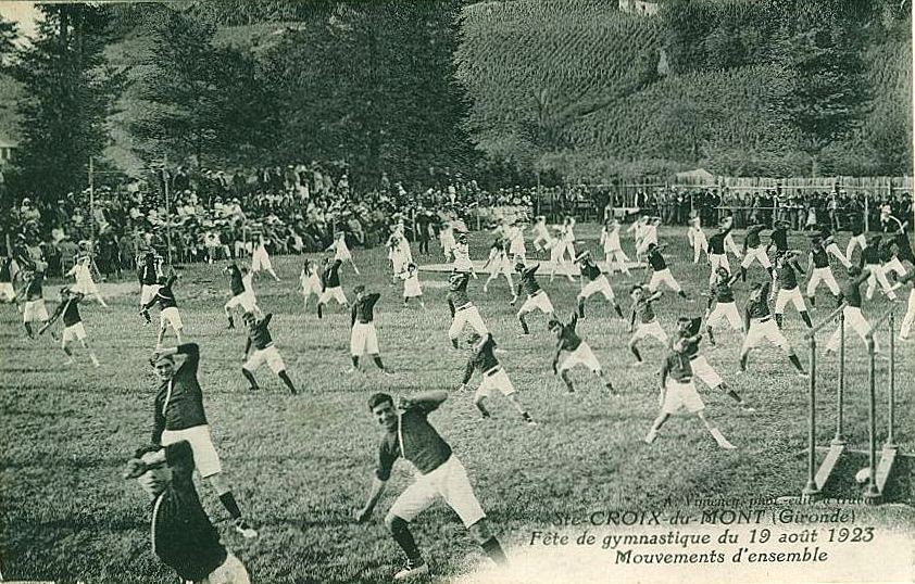 Carte postale ancienne : gymnastes en mouvements d'ensemble sur un pré, public au fond
