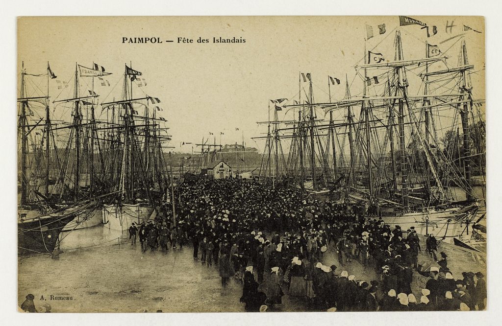 Carte postale ancienne : foule sur le quai de Paimpol entre goélettes pavoisées