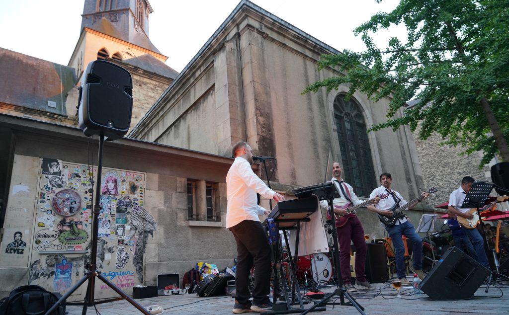 Groupe de musiciens en concert sur une place pavée devant une église en pierre