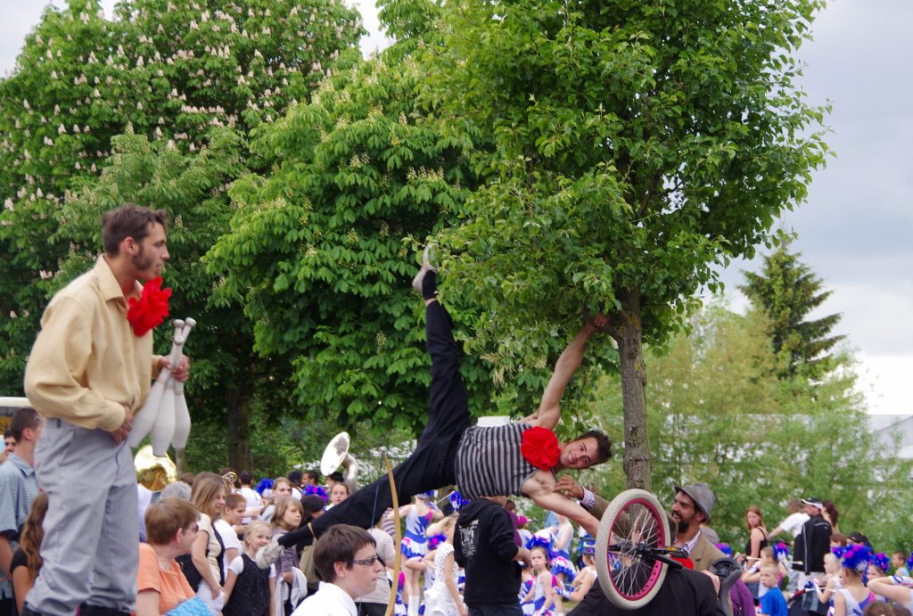Acrobates de rue en équilibre au-dessus de la foule, monocycle et arbres en fleurs
