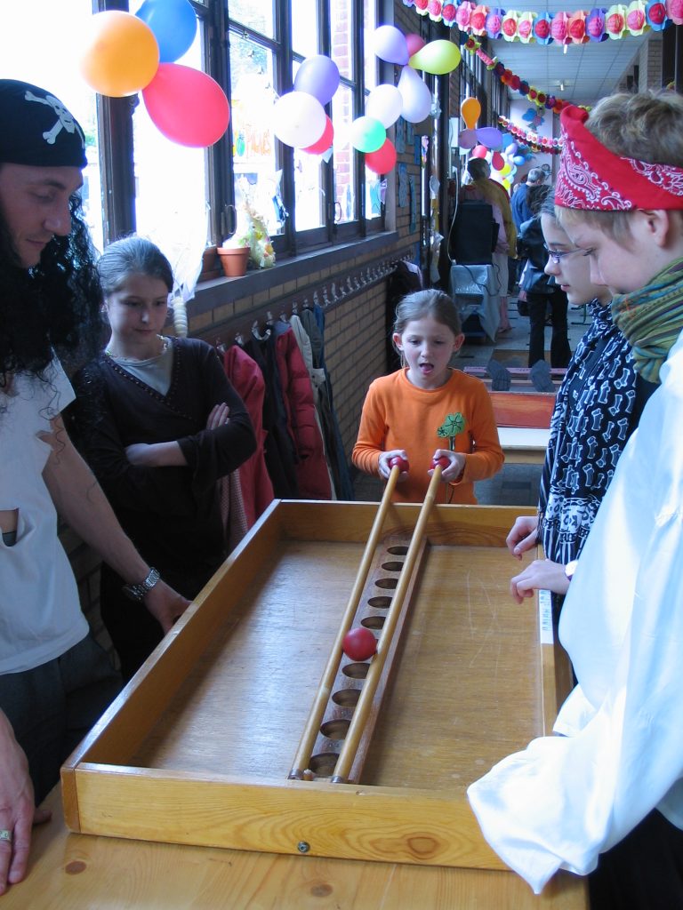 Enfants et adultes déguisés jouant à un jeu en bois traditionnel sous des ballons