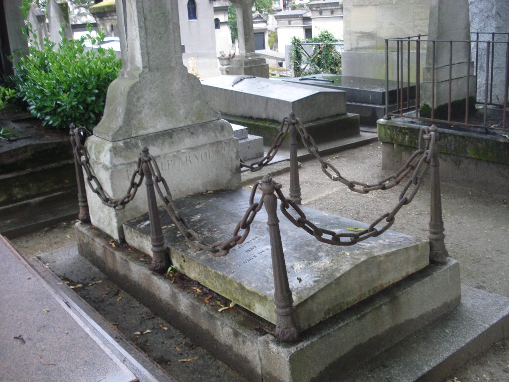 Vieille sépulture en pierre entourée de chaînes rouillées sur bornes, dans un cimetière