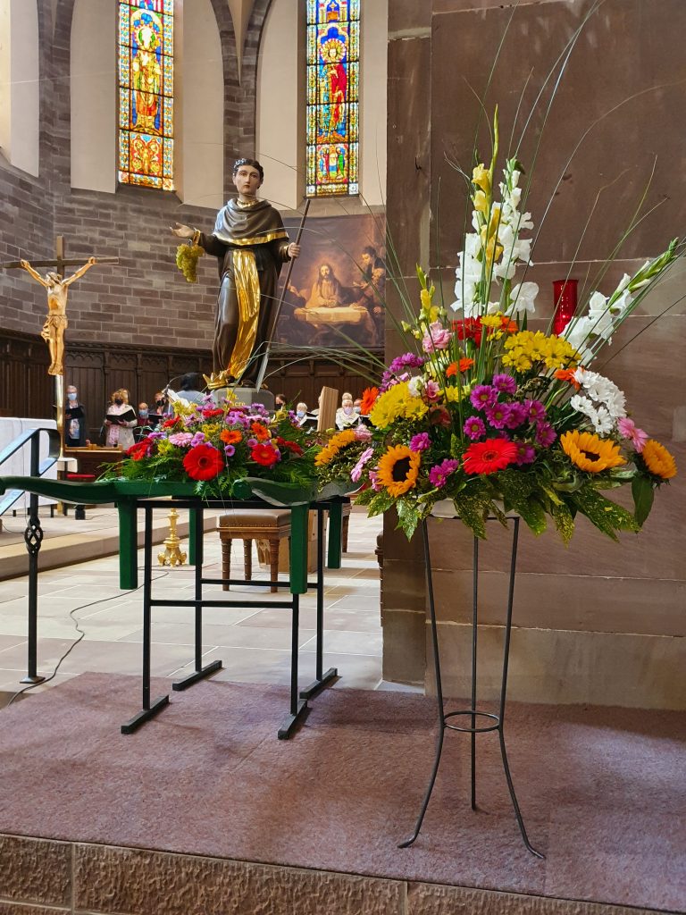 Compositions florales colorées sur pieds devant une statue de saint dans une église