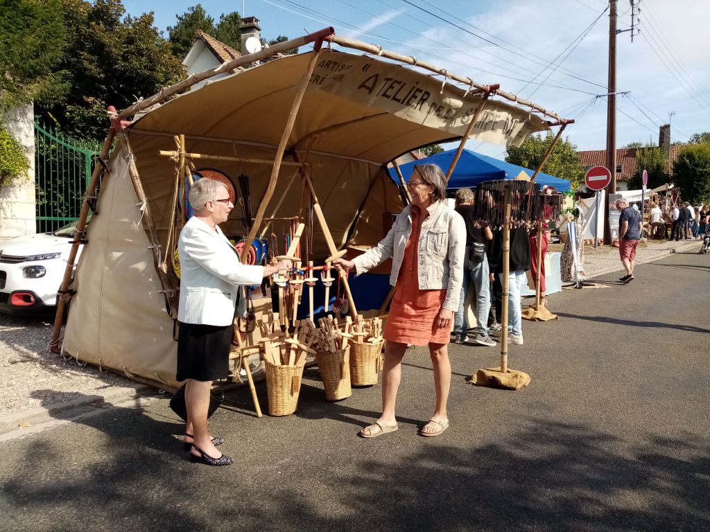 Deux visiteuses devant un stand d'artisan en bois, sous une tente de marché villageois