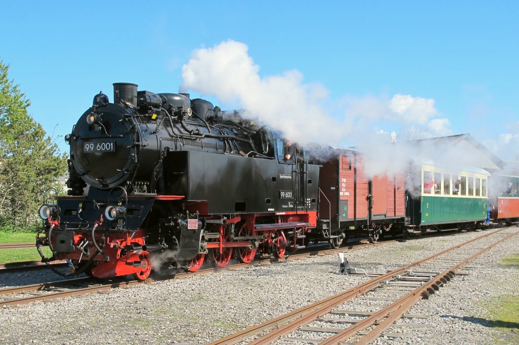 Locomotive à vapeur noire et rouge tractant wagons verts sur voie ferrée, ciel bleu