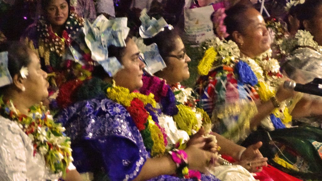 Personnes assises en tenues traditionnelles, colliers de fleurs et couronnes de billets, le soir