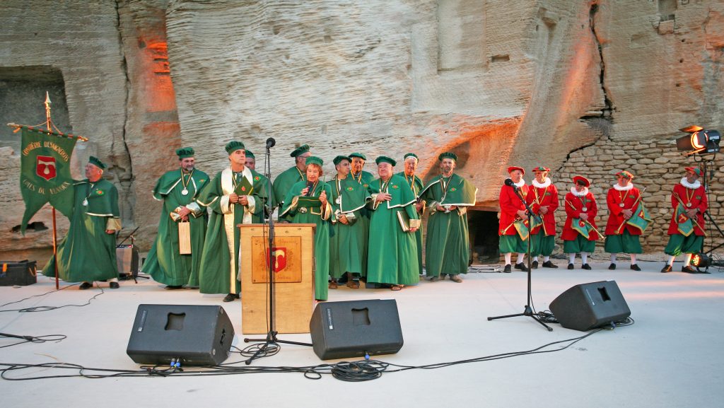Confrérie en robes vertes et rouges sur une scène devant une falaise calcaire