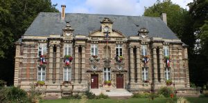 Mairie en pierre et brique pavoisée de drapeaux français, balconnières fleuries, pelouse arborée